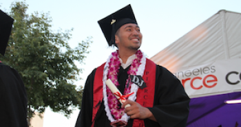 Smiling man in graduating regalia holding diploma